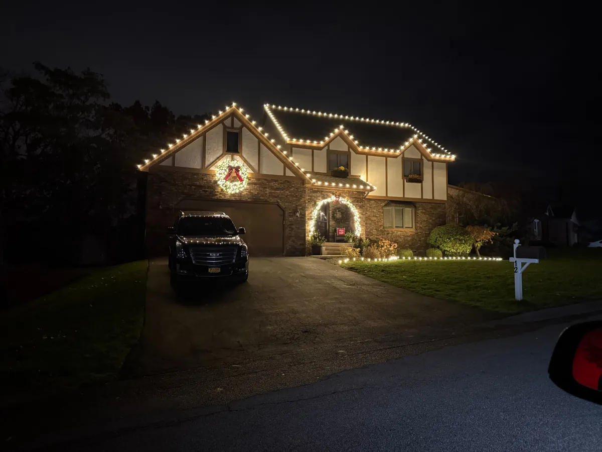 Tudor home with warm white Christmas rooflines, a wreath and a lit entry arch
